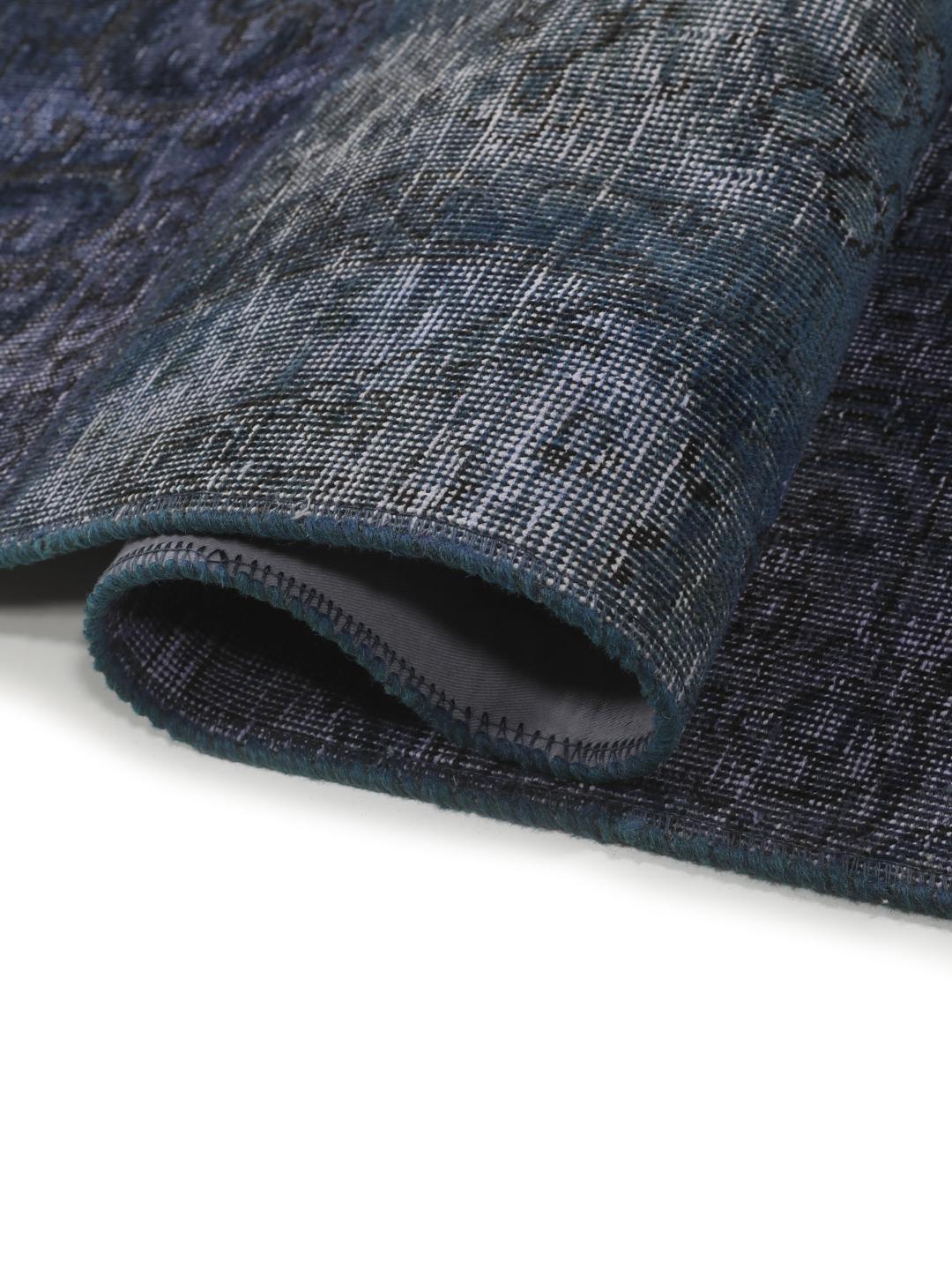 Een groot rechthoekig patchwork vloerkleed met diverse tinten donkerblauw en grijs, handgemaakt in het Midden-Oosten.