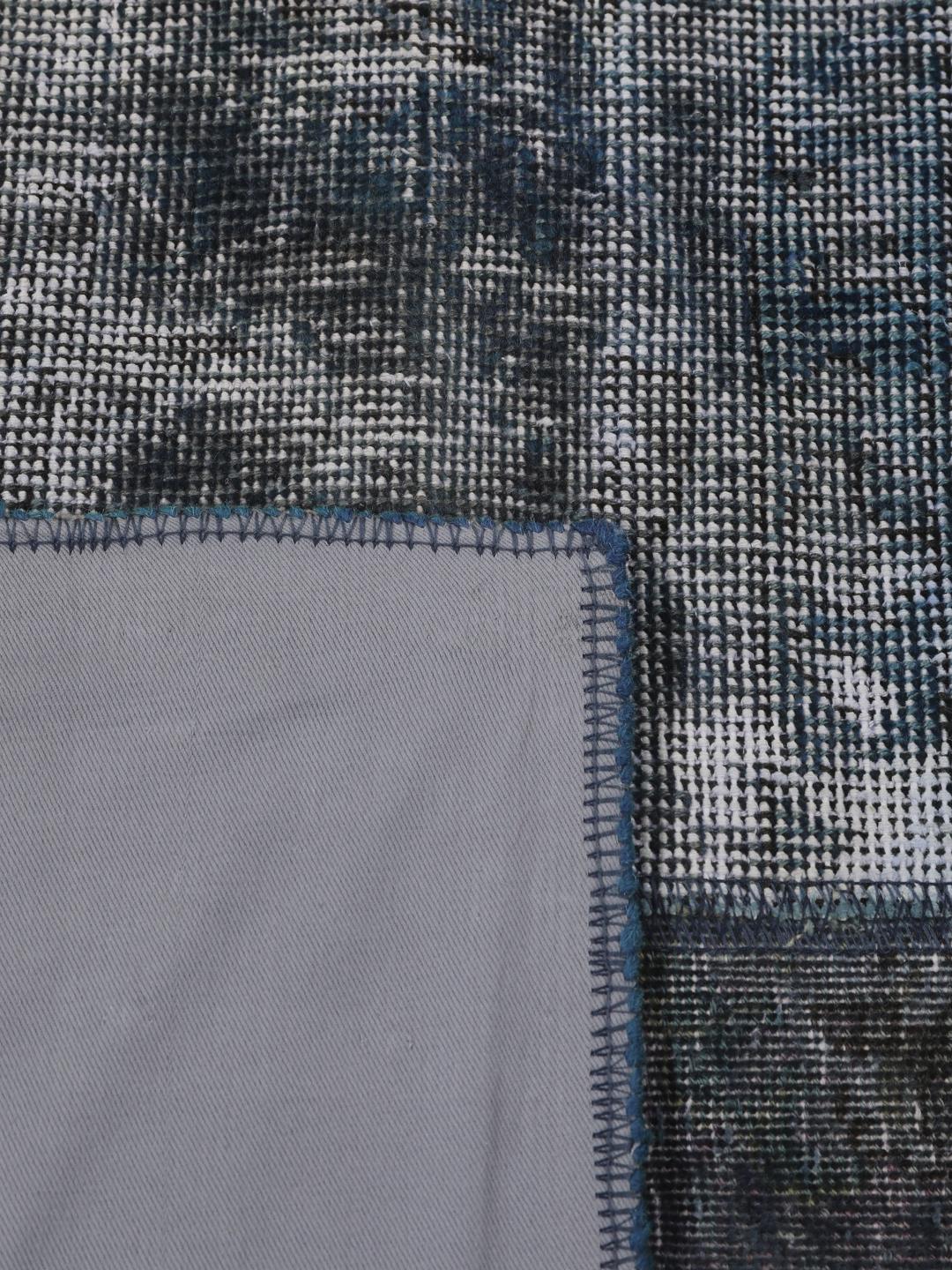 Een groot rechthoekig patchwork vloerkleed met diverse tinten donkerblauw en grijs, handgemaakt in het Midden-Oosten.