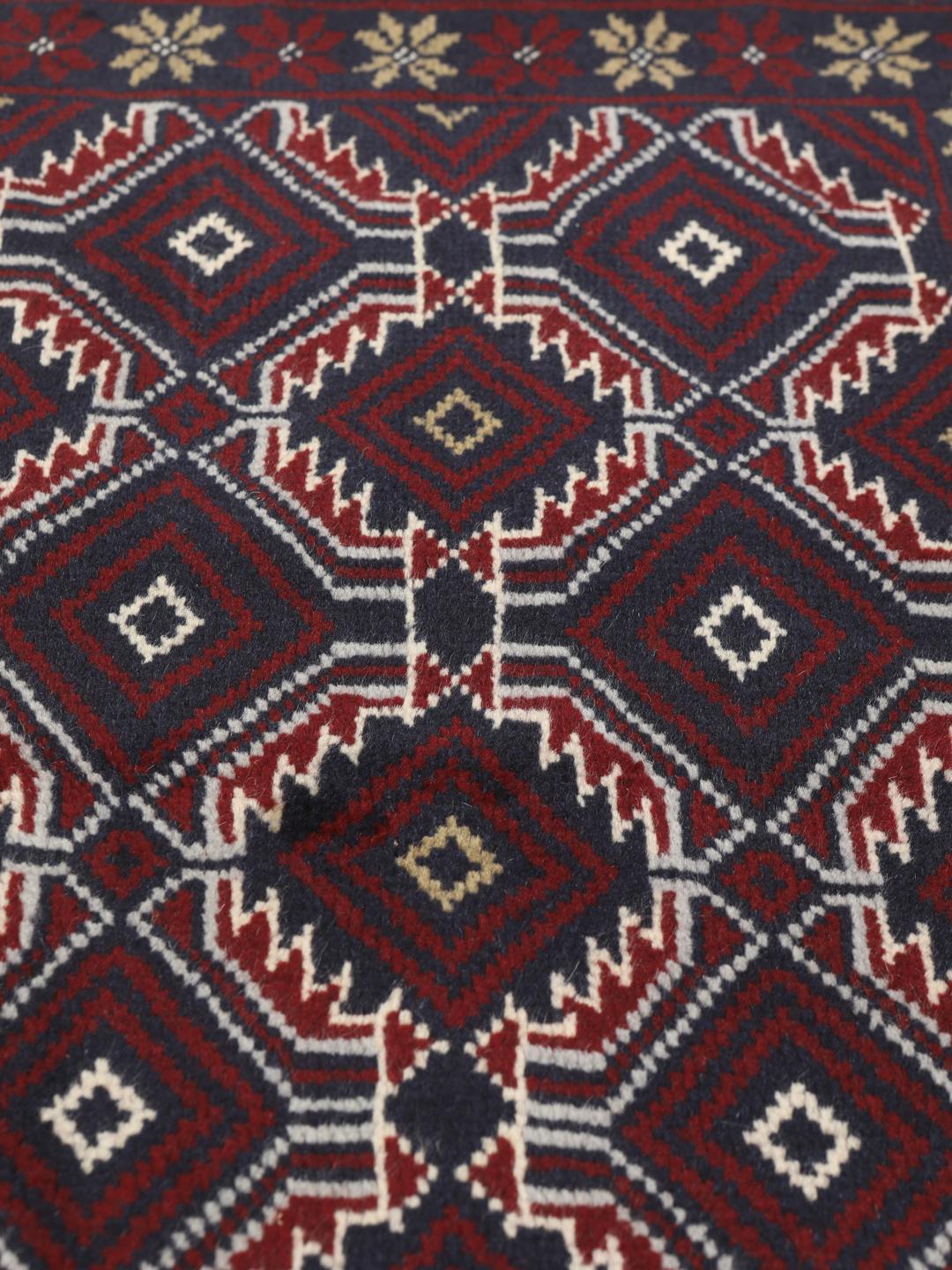 Et håndknyttet Baluch-tæppe fra Mellemøsten med et mørkerødt og blåt geometrisk design.