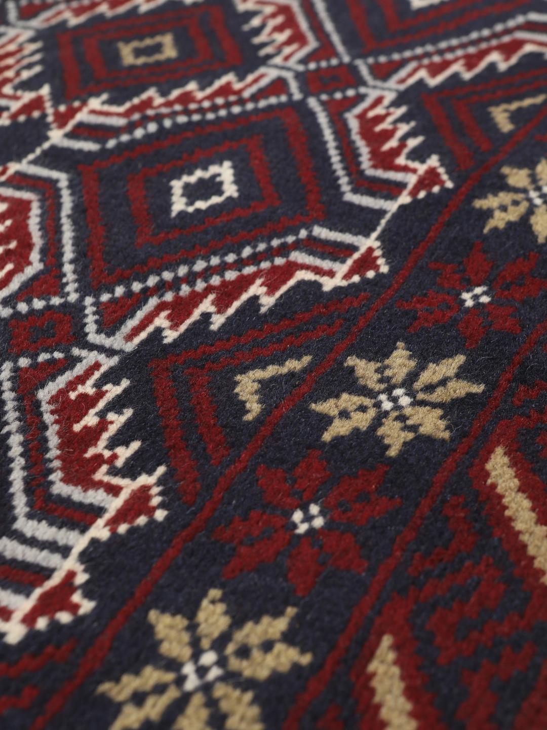 Et håndknyttet Baluch-tæppe fra Mellemøsten med et mørkerødt og blåt geometrisk design.