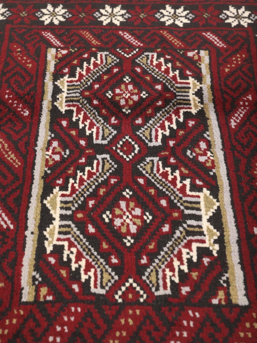 Hand-knotted Middle Eastern Beluch rug in dark red with floral and geometric patterns.
