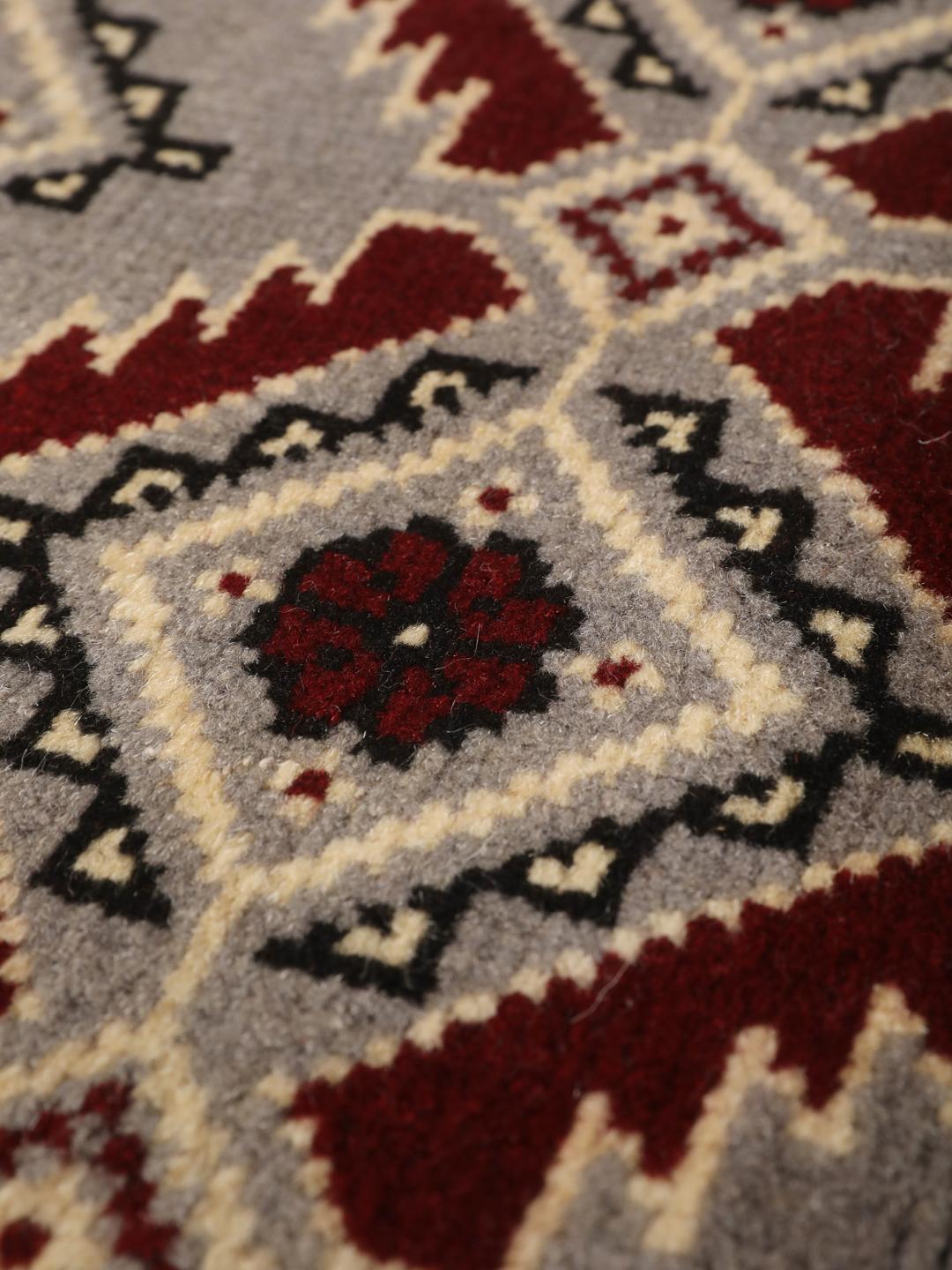 Et håndknyttet Baluch-tæppe fra Mellemøsten i nuancer af grå og rød.