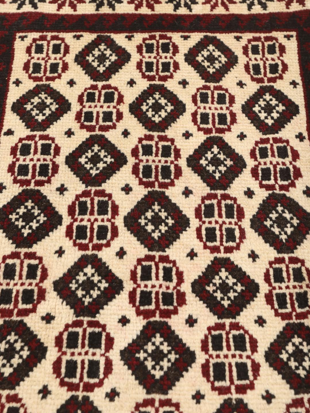 A hand-knotted Baluch rug from the Middle East featuring a red and beige geometric pattern.