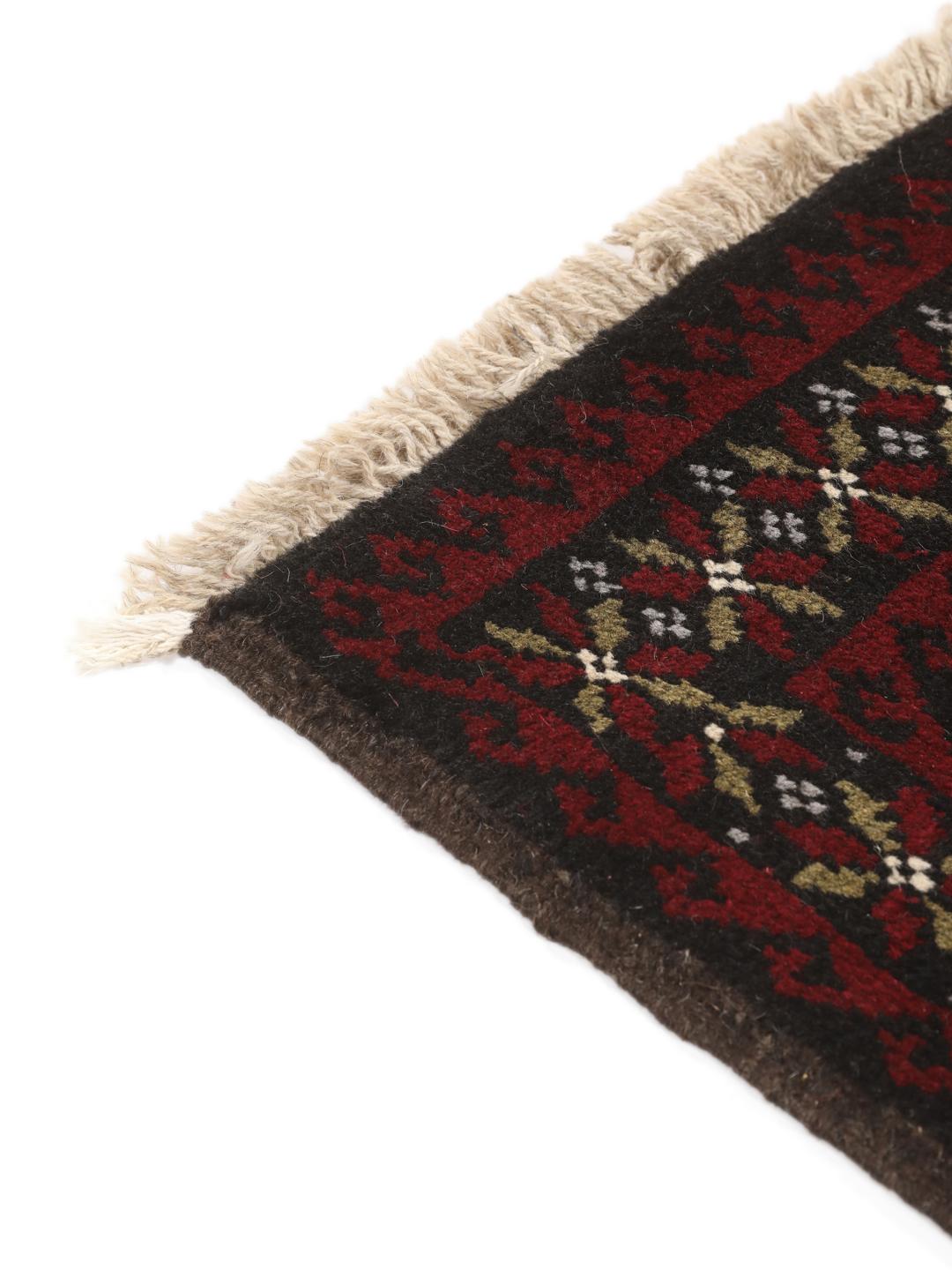 A small, hand-knotted Beluch rug from the Middle East featuring geometric patterns in dark red and black.