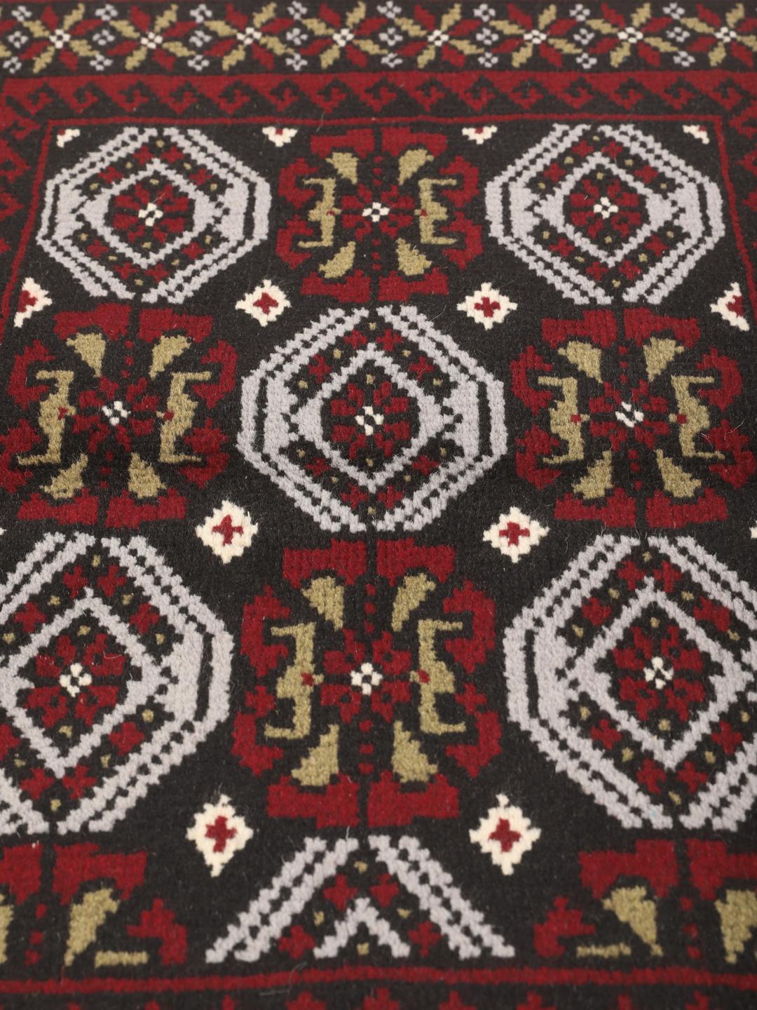 A small, hand-knotted Beluch rug from the Middle East featuring geometric patterns in dark red and black.