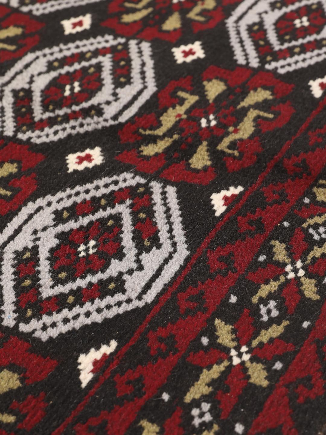 A small, hand-knotted Beluch rug from the Middle East featuring geometric patterns in dark red and black.