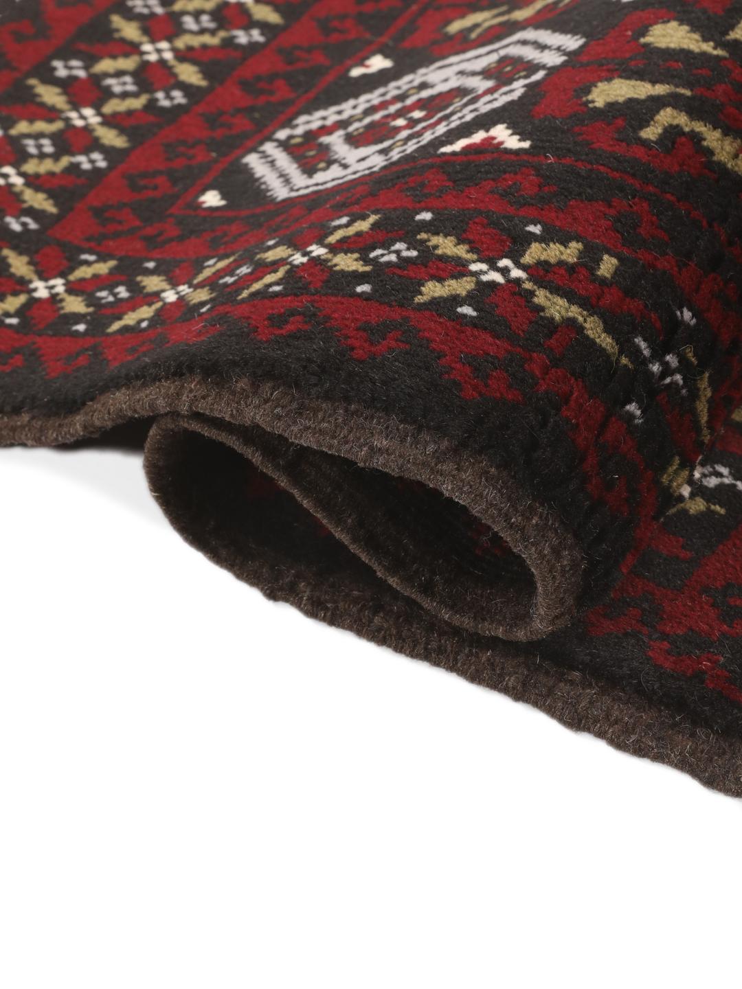 A small, hand-knotted Beluch rug from the Middle East featuring geometric patterns in dark red and black.