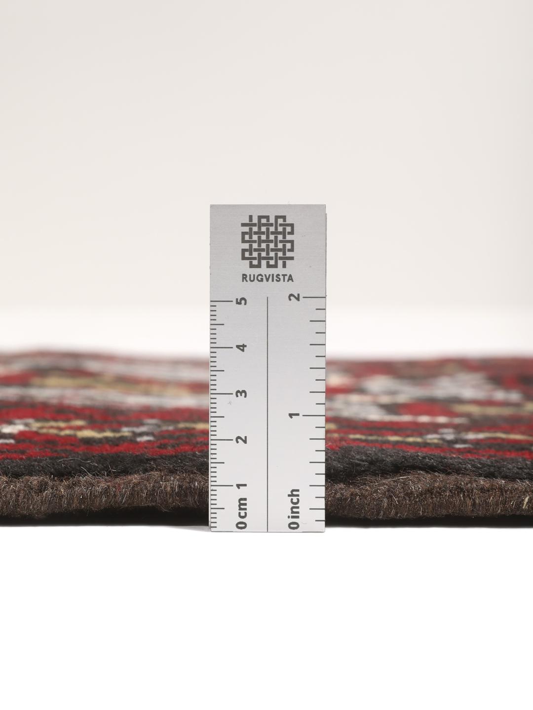 A small, hand-knotted Beluch rug from the Middle East featuring geometric patterns in dark red and black.