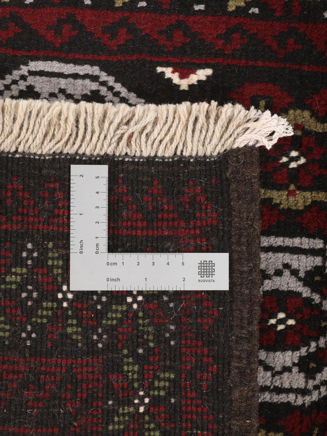 A small, hand-knotted Beluch rug from the Middle East featuring geometric patterns in dark red and black.