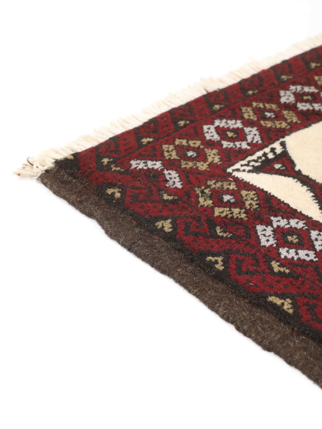 Et håndknyttet Baluch-tæppe fra Mellemøsten med et mørkerødt og cremefarvet geometrisk design.
