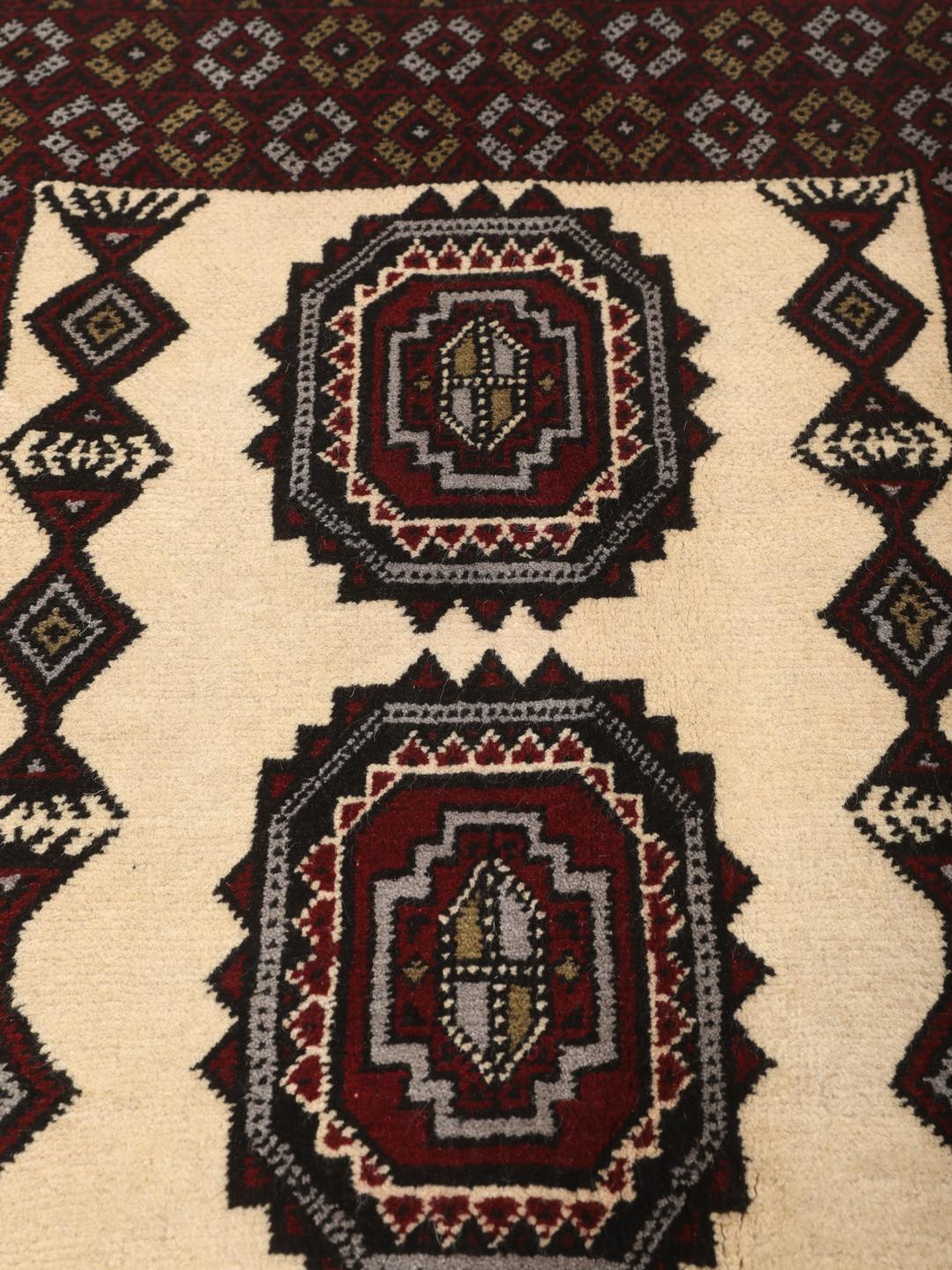 Et håndknyttet Baluch-tæppe fra Mellemøsten med et mørkerødt og cremefarvet geometrisk design.