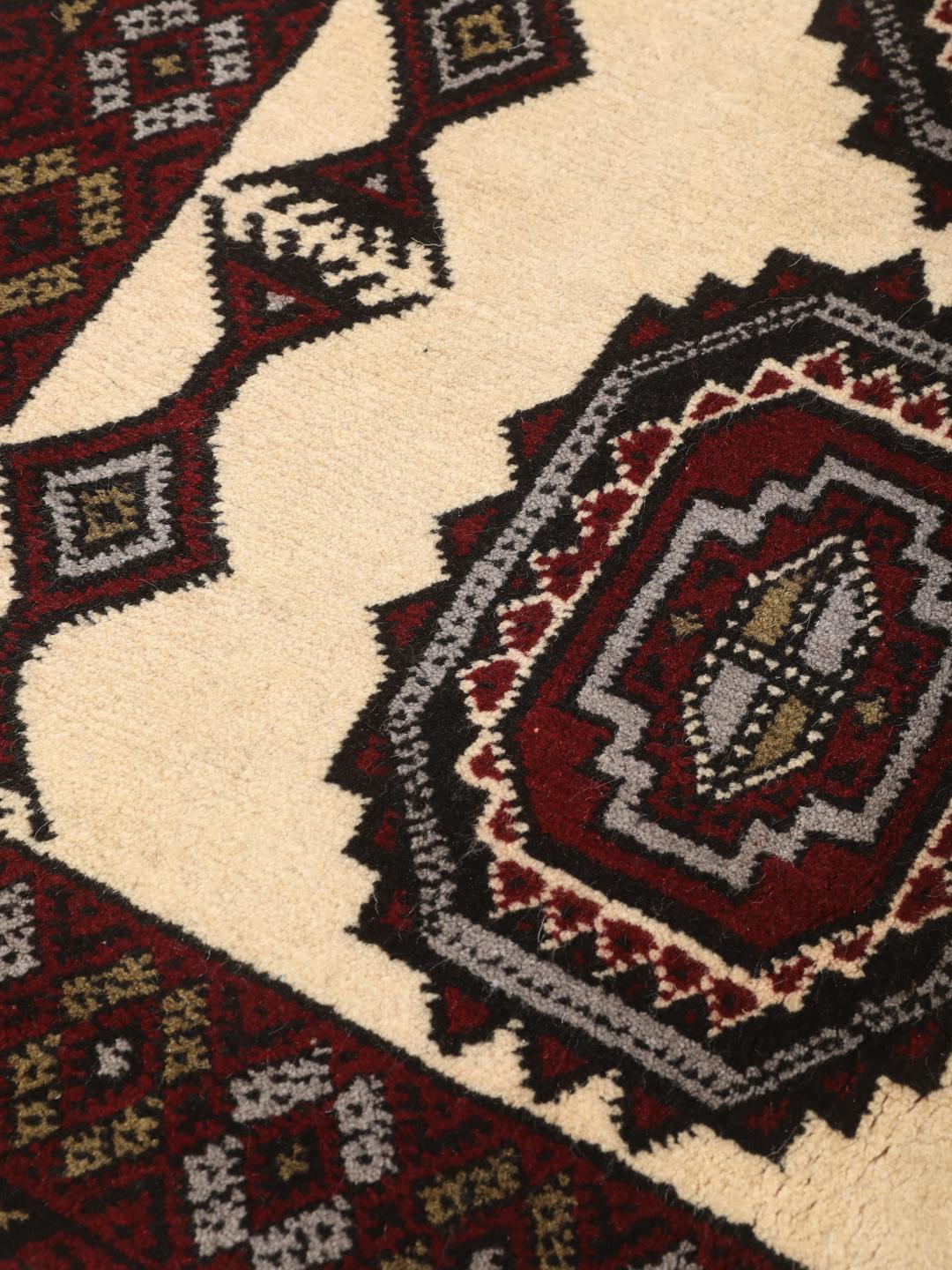 Et håndknyttet Baluch-tæppe fra Mellemøsten med et mørkerødt og cremefarvet geometrisk design.