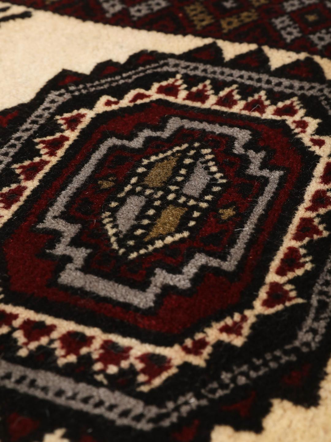 Et håndknyttet Baluch-tæppe fra Mellemøsten med et mørkerødt og cremefarvet geometrisk design.