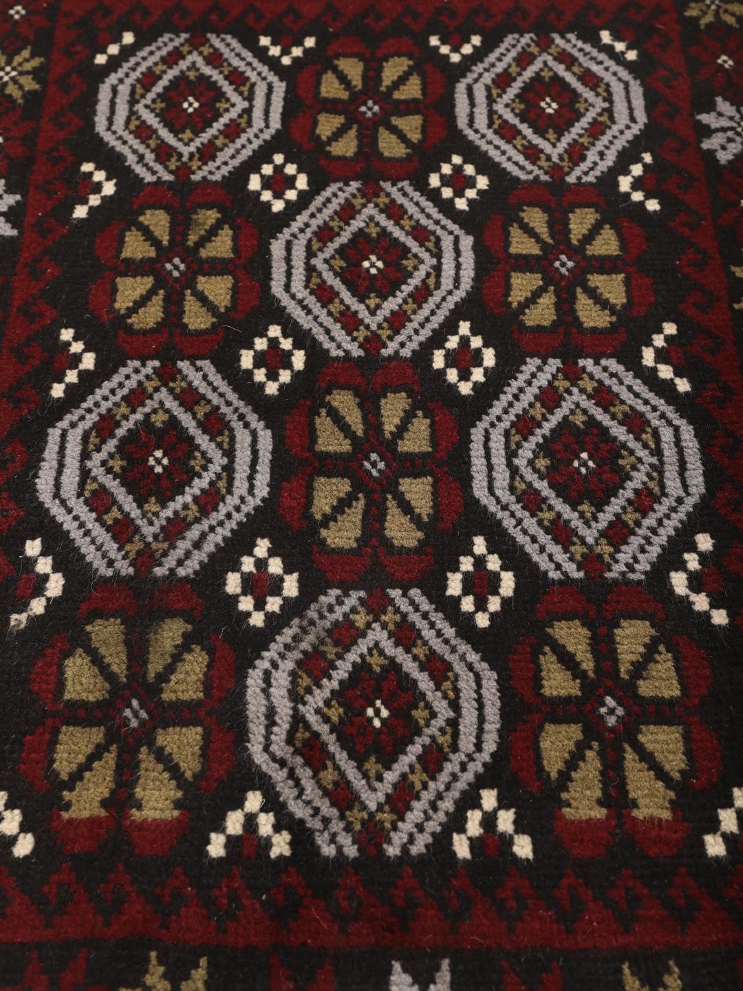 Et håndknyttet Baluch-tæppe fra Mellemøsten med et levende rødt og mørkt felt med geometriske mønstre.