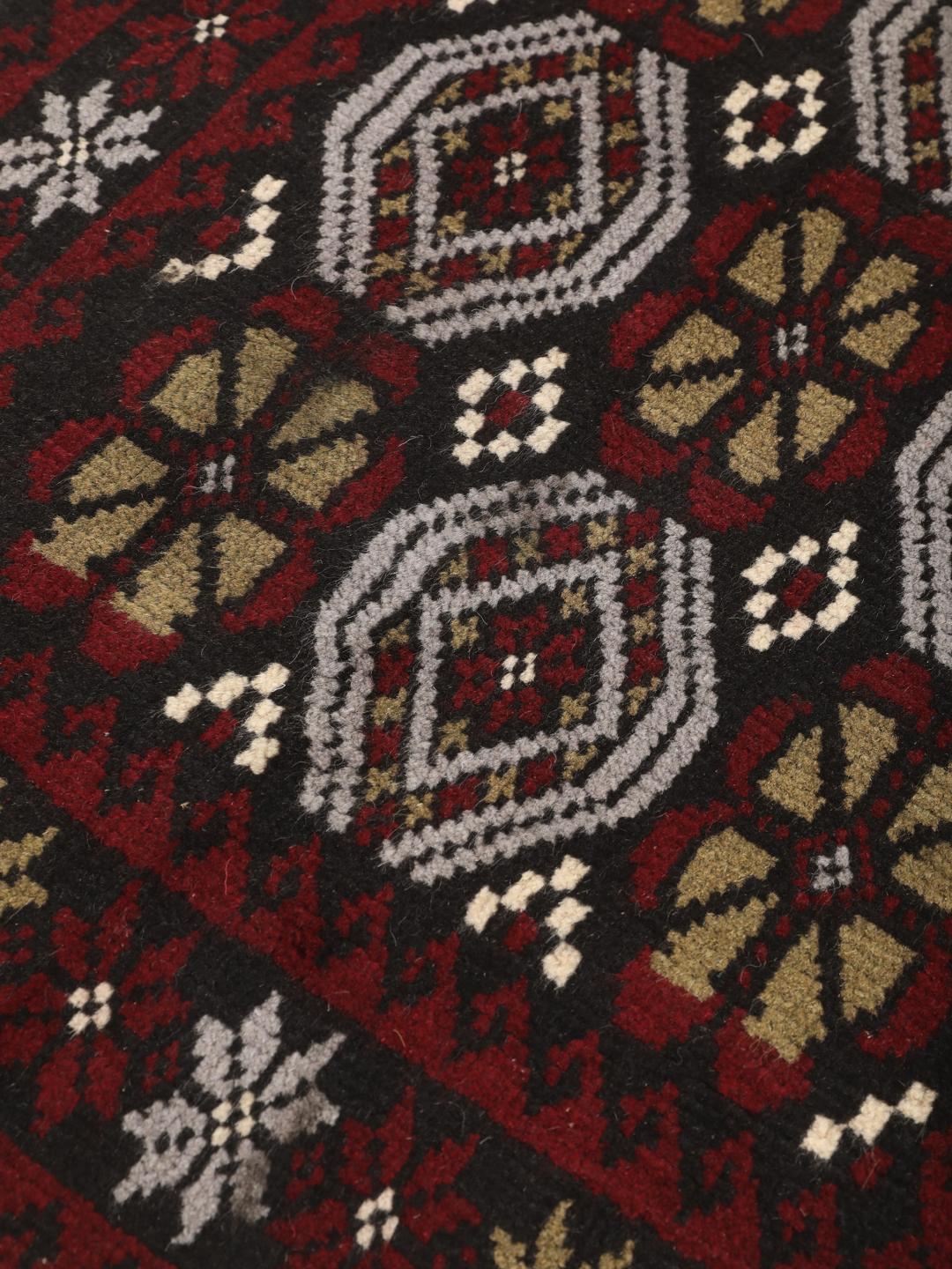 Et håndknyttet Baluch-tæppe fra Mellemøsten med et levende rødt og mørkt felt med geometriske mønstre.