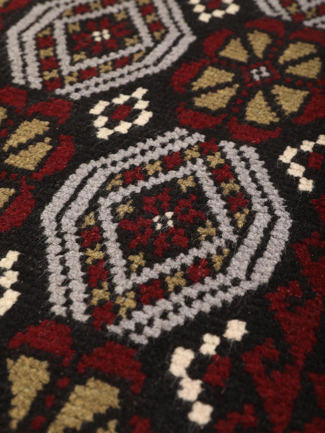Et håndknyttet Baluch-tæppe fra Mellemøsten med et levende rødt og mørkt felt med geometriske mønstre.