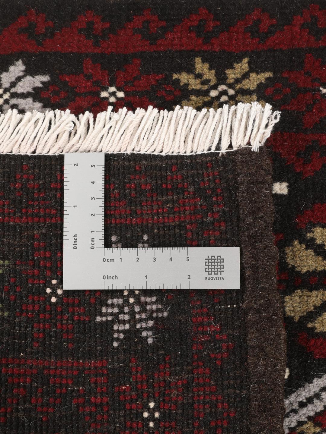 Et håndknyttet Baluch-tæppe fra Mellemøsten med et levende rødt og mørkt felt med geometriske mønstre.