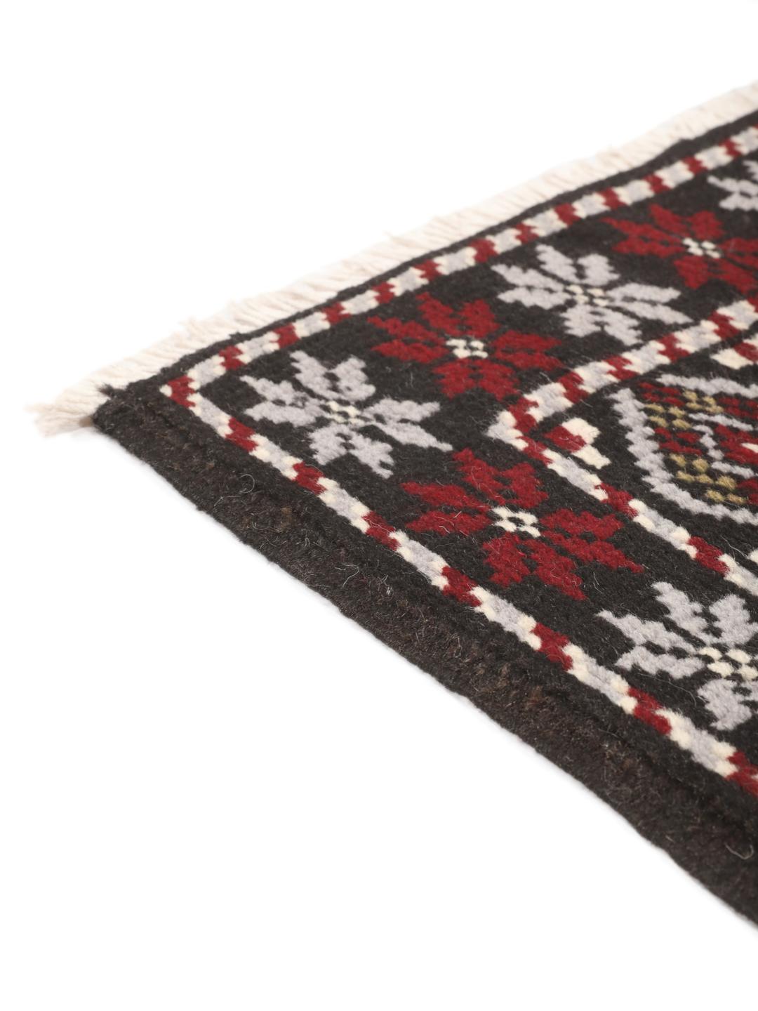 A hand-knotted Baluch rug from the Middle East featuring a black, red, and grey geometric pattern.