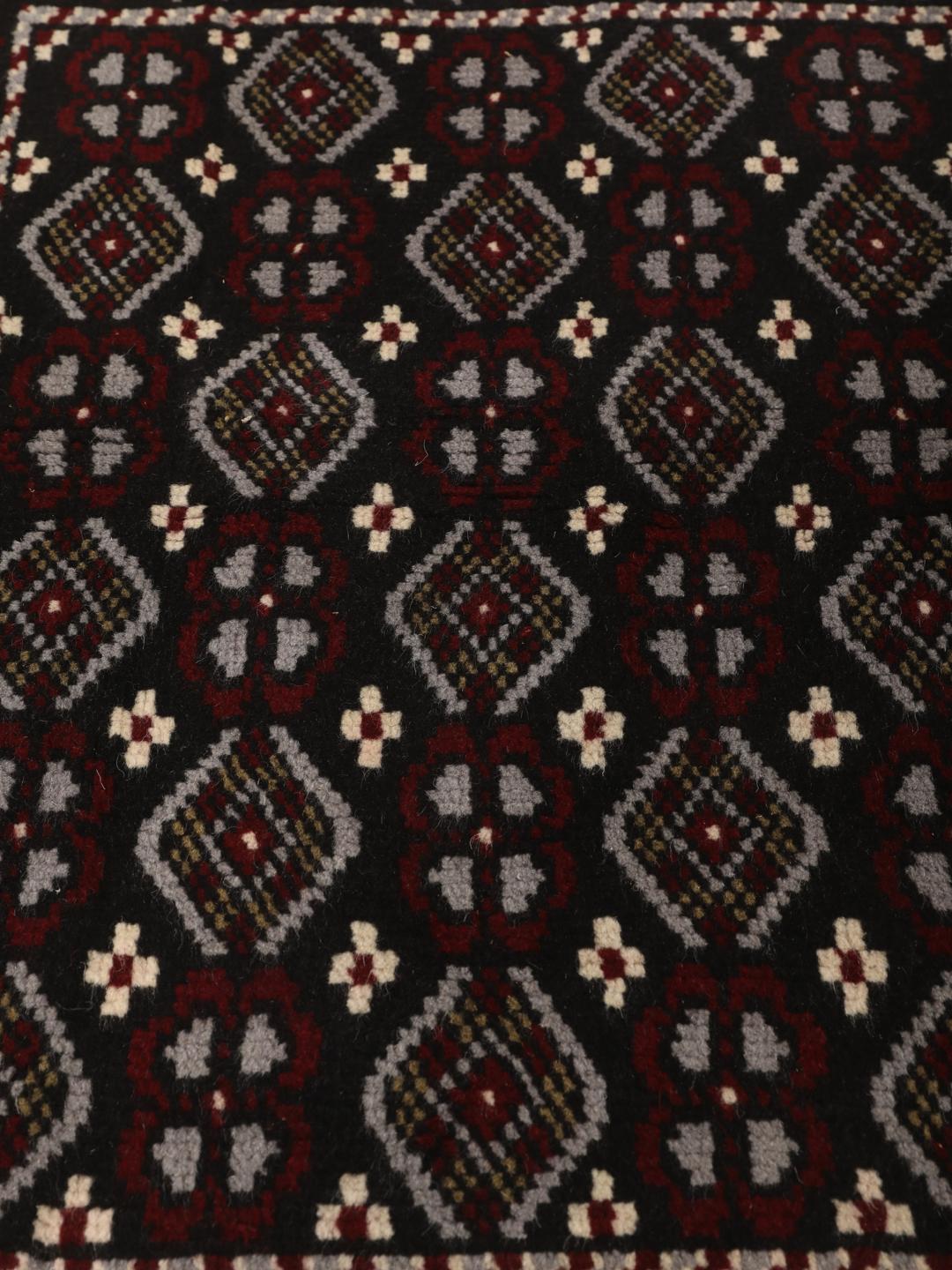 A hand-knotted Baluch rug from the Middle East featuring a black, red, and grey geometric pattern.