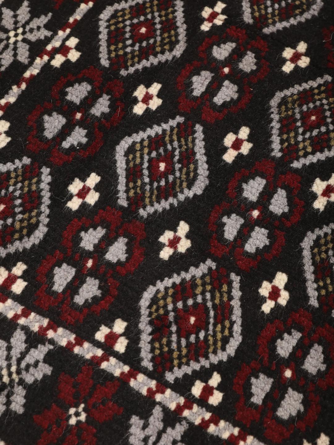 A hand-knotted Baluch rug from the Middle East featuring a black, red, and grey geometric pattern.