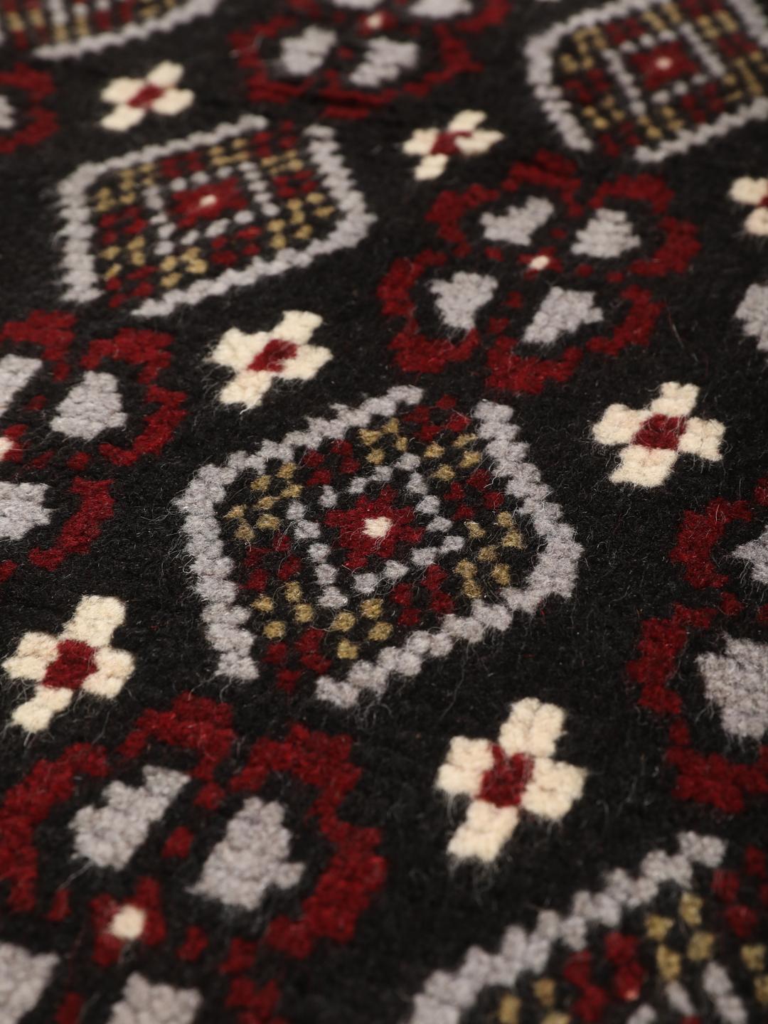 A hand-knotted Baluch rug from the Middle East featuring a black, red, and grey geometric pattern.