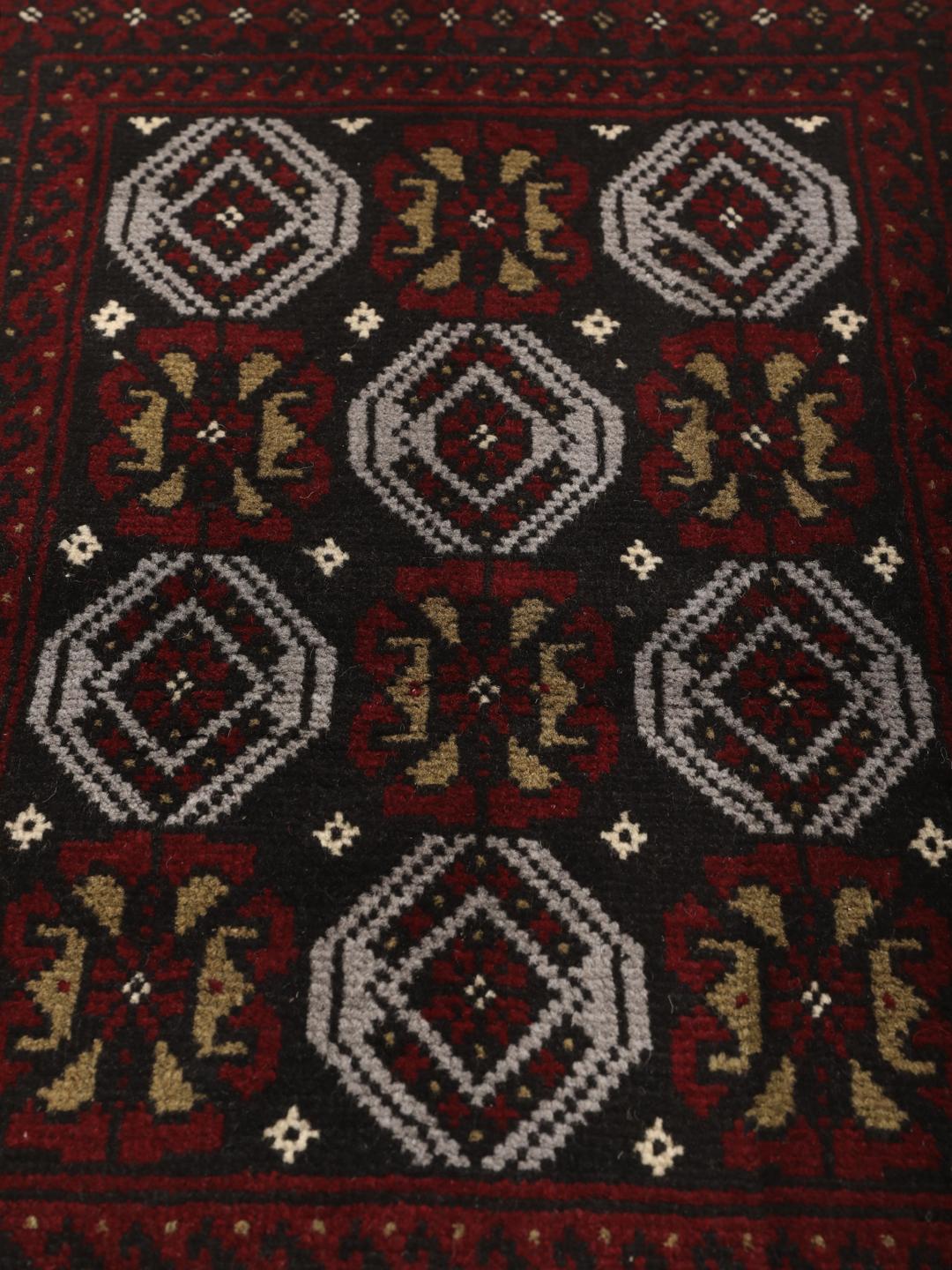 A small, one-of-a-kind Baluch rug from the Middle East with a dark-red and black geometric pattern.