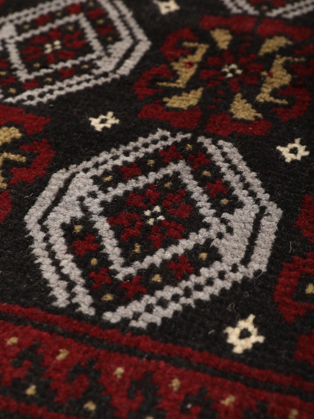 A small, one-of-a-kind Baluch rug from the Middle East with a dark-red and black geometric pattern.