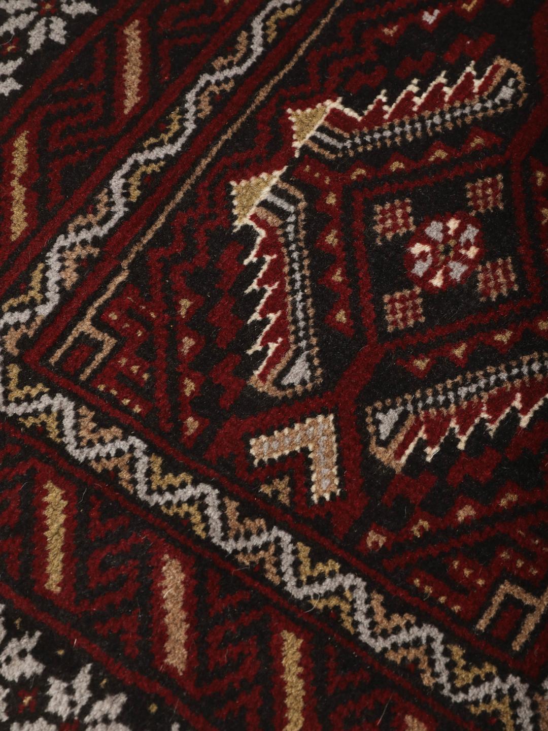 Et håndknyttet Baluch-tæppe fra Mellemøsten i mørkerøde og sorte toner.