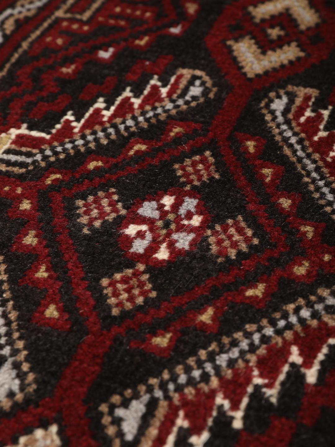 Et håndknyttet Baluch-tæppe fra Mellemøsten i mørkerøde og sorte toner.