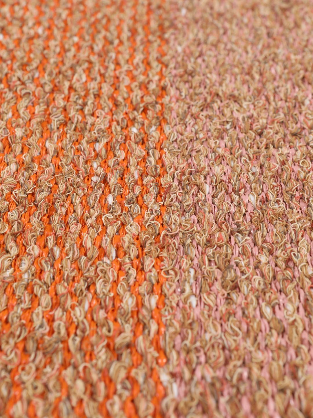 Een rechthoekig tapijt met koraalrode, oranje en beige gestreepte patronen met geometrische accenten.