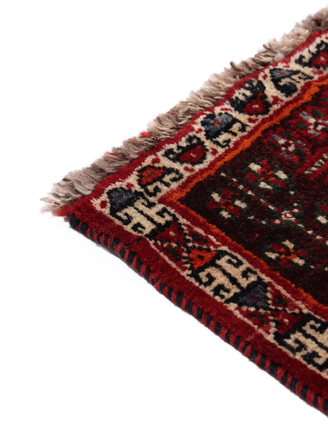 A hand-knotted Middle Eastern Ghashghai rug in red and dark tones with geometric patterns.