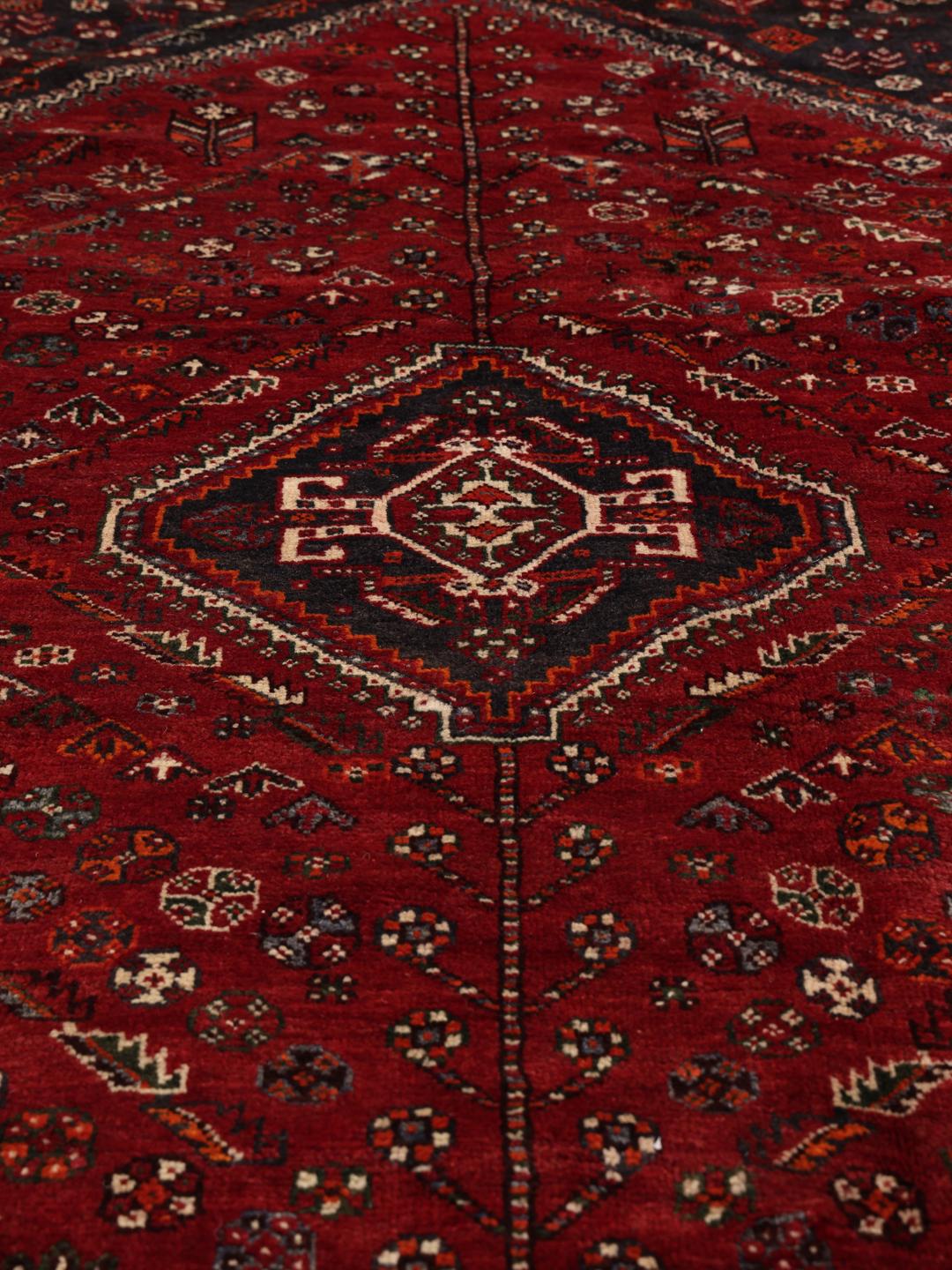 A hand-knotted Middle Eastern Ghashghai rug in red and dark tones with geometric patterns.