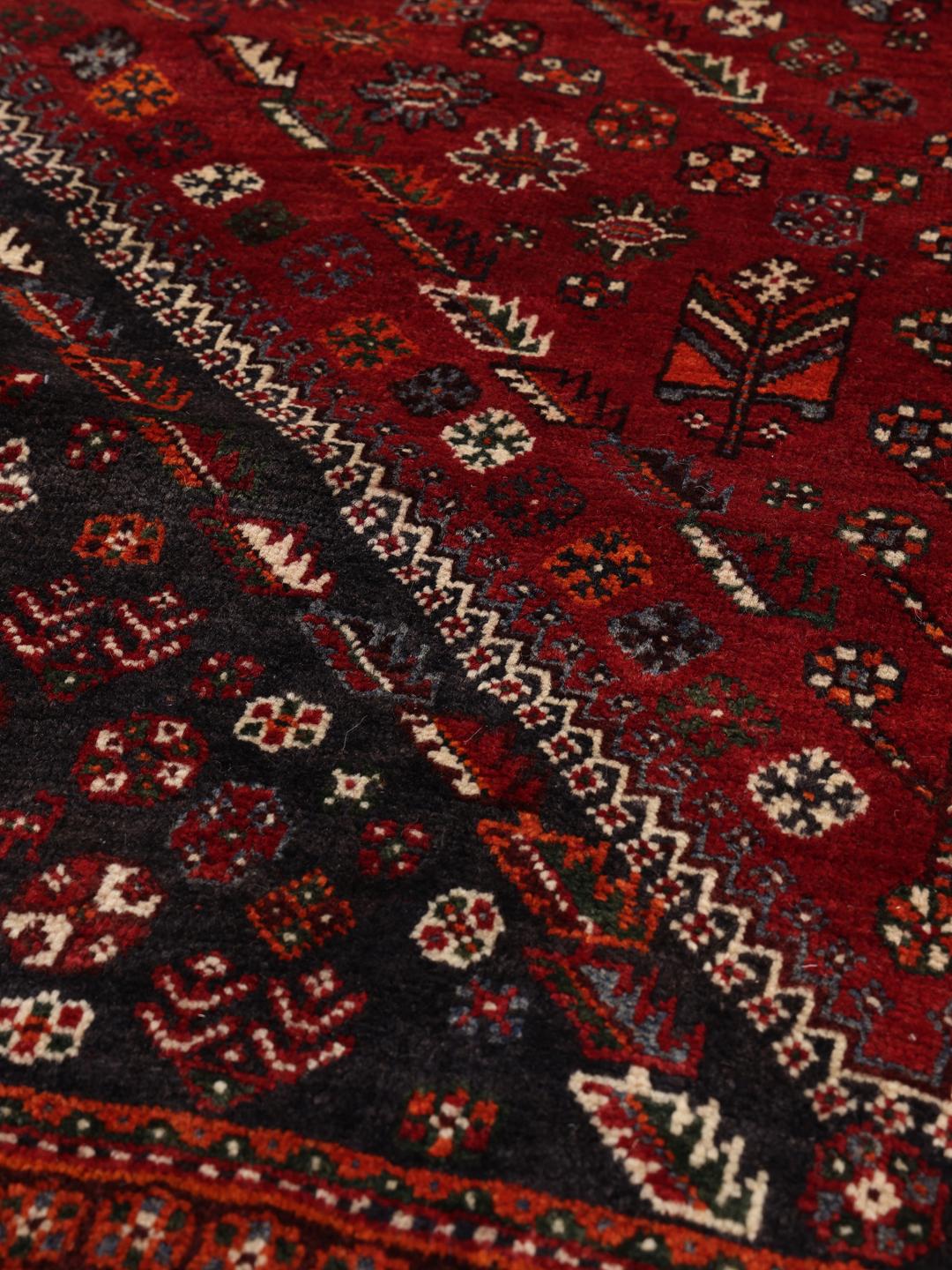 A hand-knotted Middle Eastern Ghashghai rug in red and dark tones with geometric patterns.