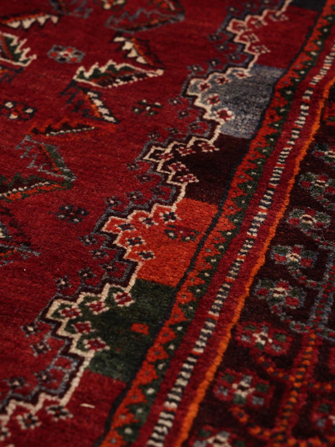 A hand-knotted Middle Eastern Ghashghai rug in red and dark tones with geometric patterns.