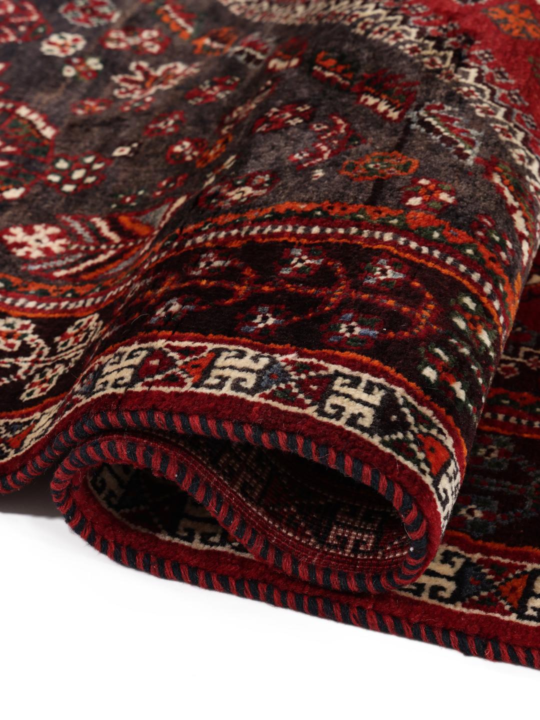 A hand-knotted Middle Eastern Ghashghai rug in red and dark tones with geometric patterns.