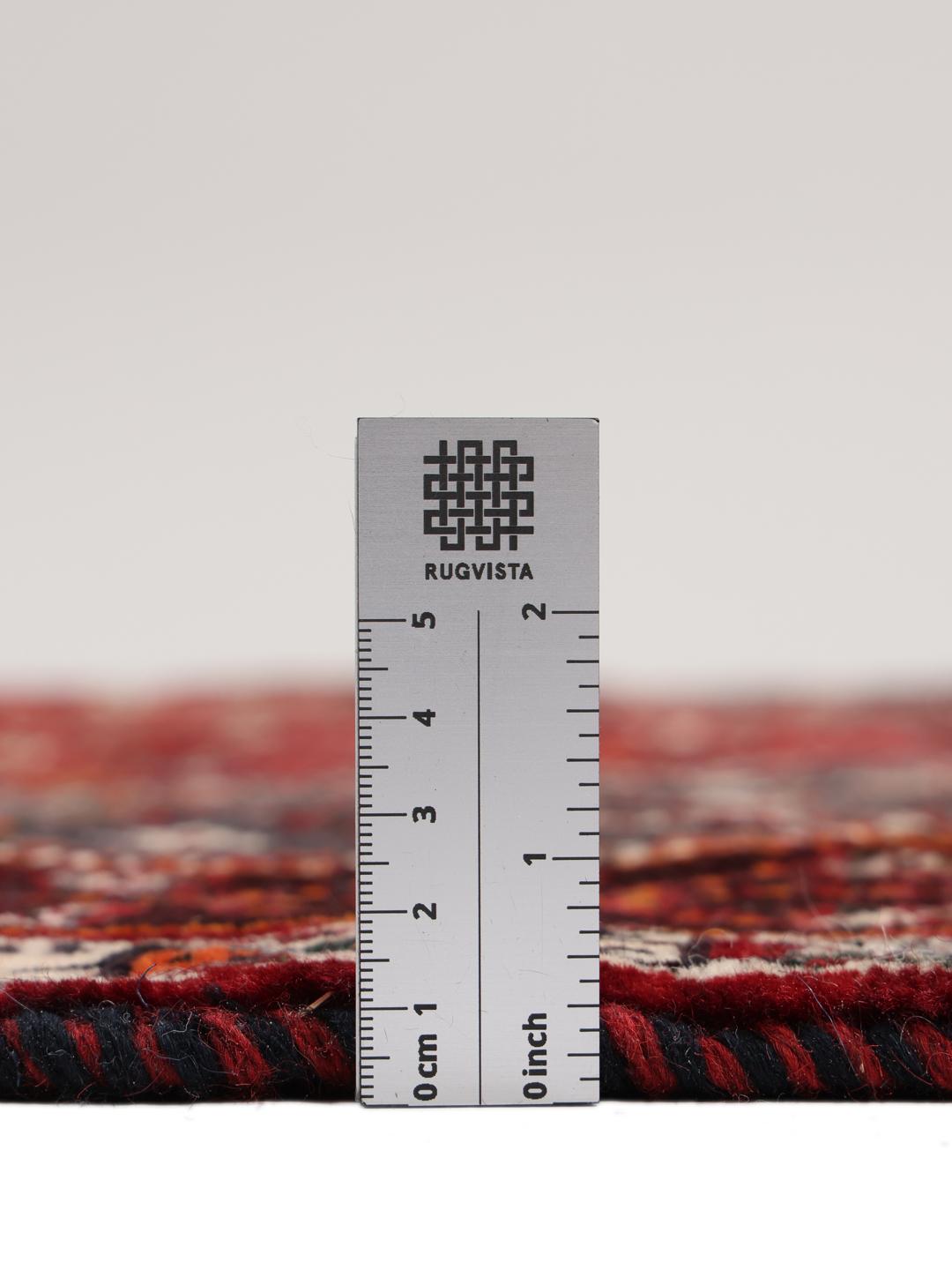 A hand-knotted Middle Eastern Ghashghai rug in red and dark tones with geometric patterns.