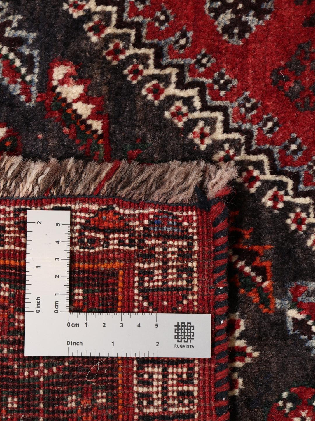 A hand-knotted Middle Eastern Ghashghai rug in red and dark tones with geometric patterns.