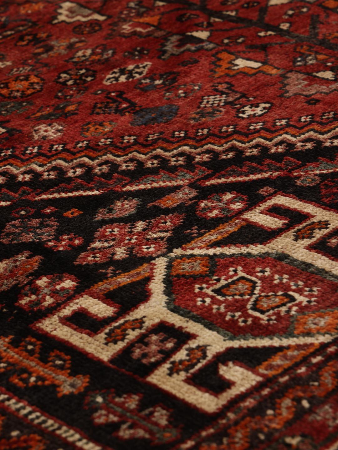A hand-knotted Ghashghai rug from the Middle East in shades of red and black.