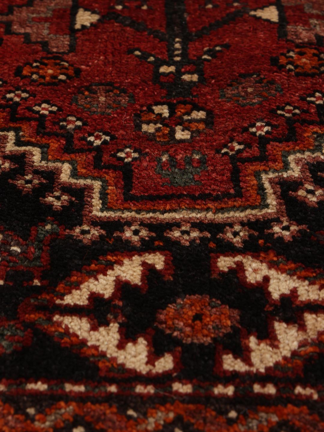 A hand-knotted Ghashghai rug from the Middle East in shades of red and black.