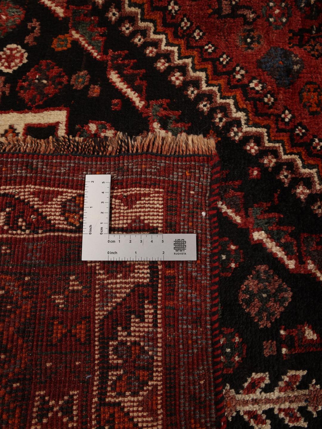 A hand-knotted Ghashghai rug from the Middle East in shades of red and black.