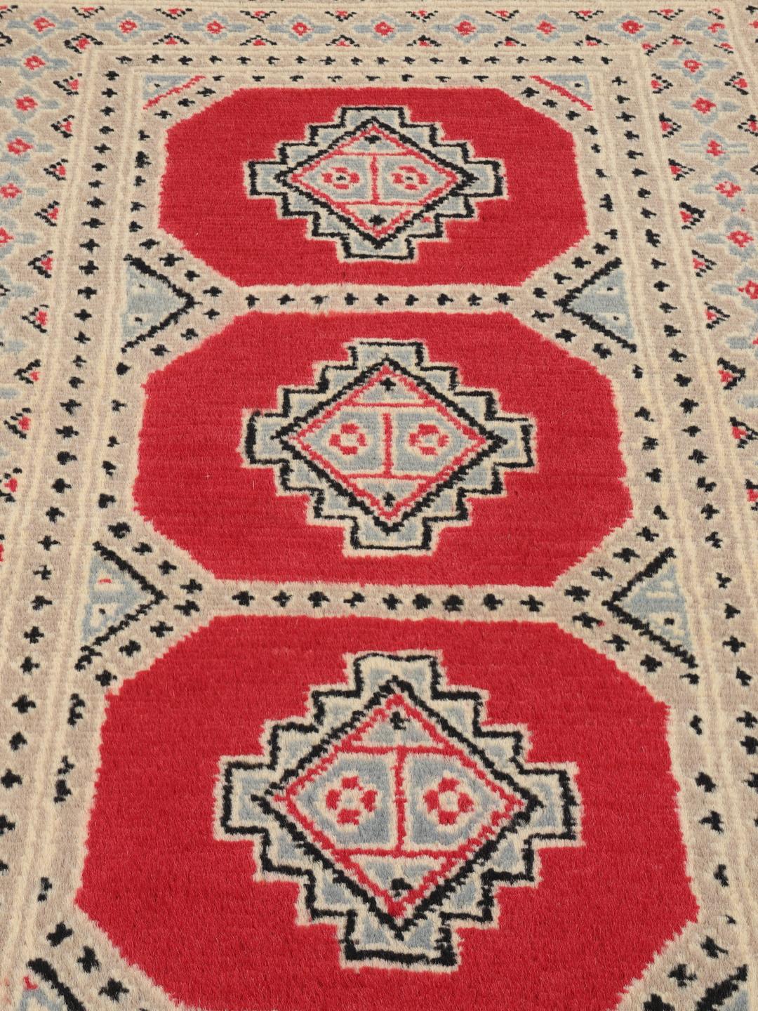 A hand-knotted Pakistan Bokhara 2ply rug with a red field and geometric motifs.