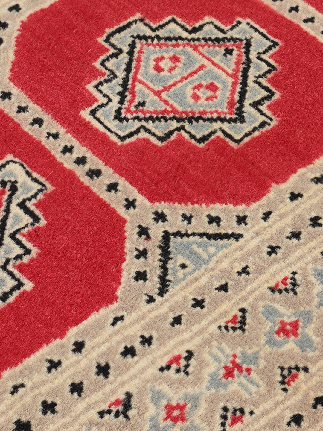 A hand-knotted Pakistan Bokhara 2ply rug with a red field and geometric motifs.