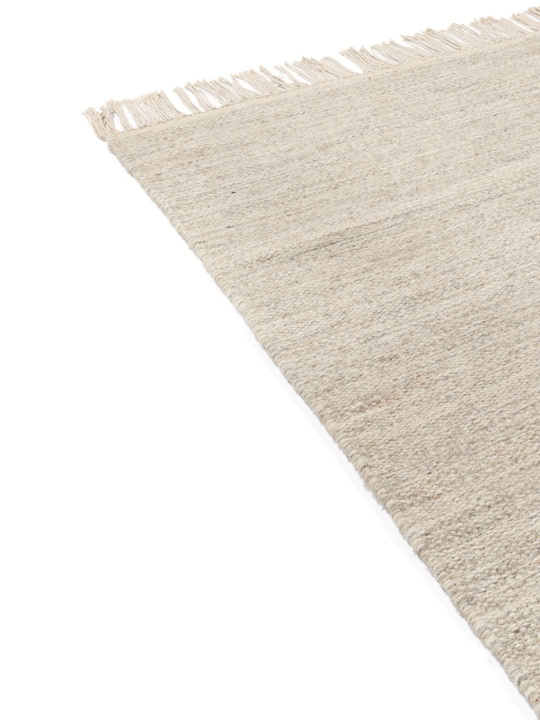 Beige tapijt met een handgeweven textuur en afgewerkt met franjes aan de uiteinden