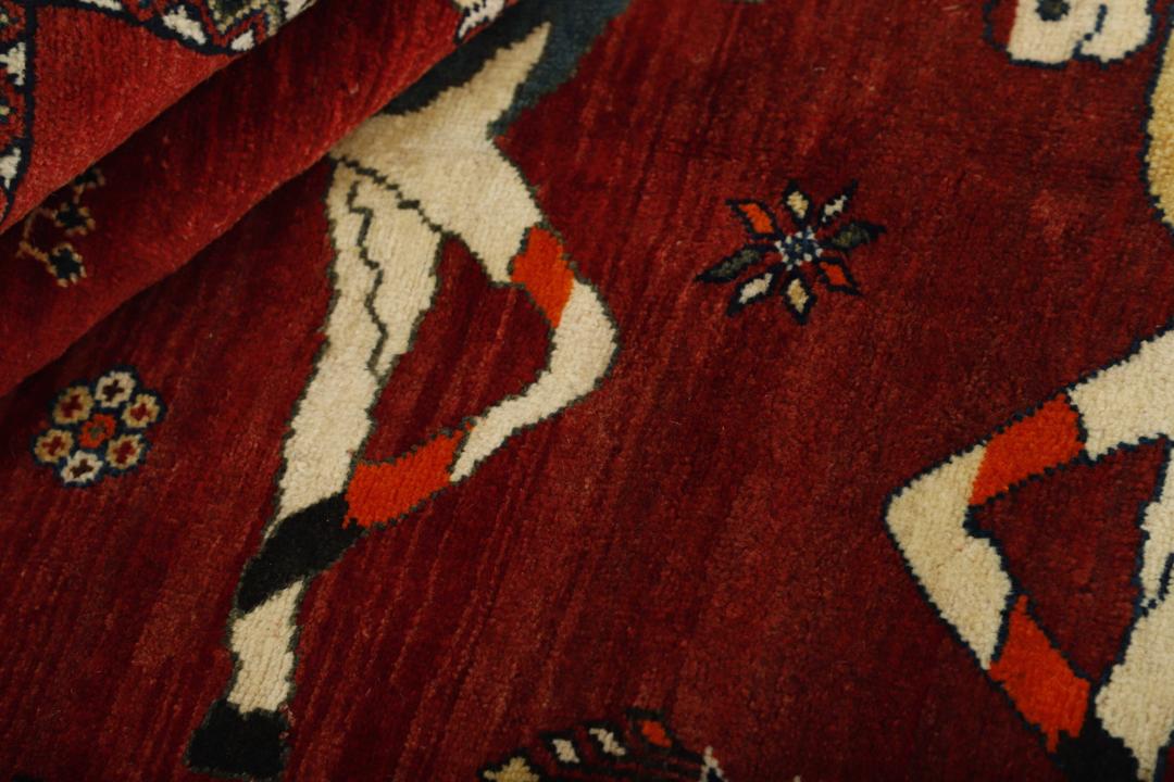 A hand-knotted Kashghai rug from the Middle East with a red field, featuring horse and butterfly motifs.