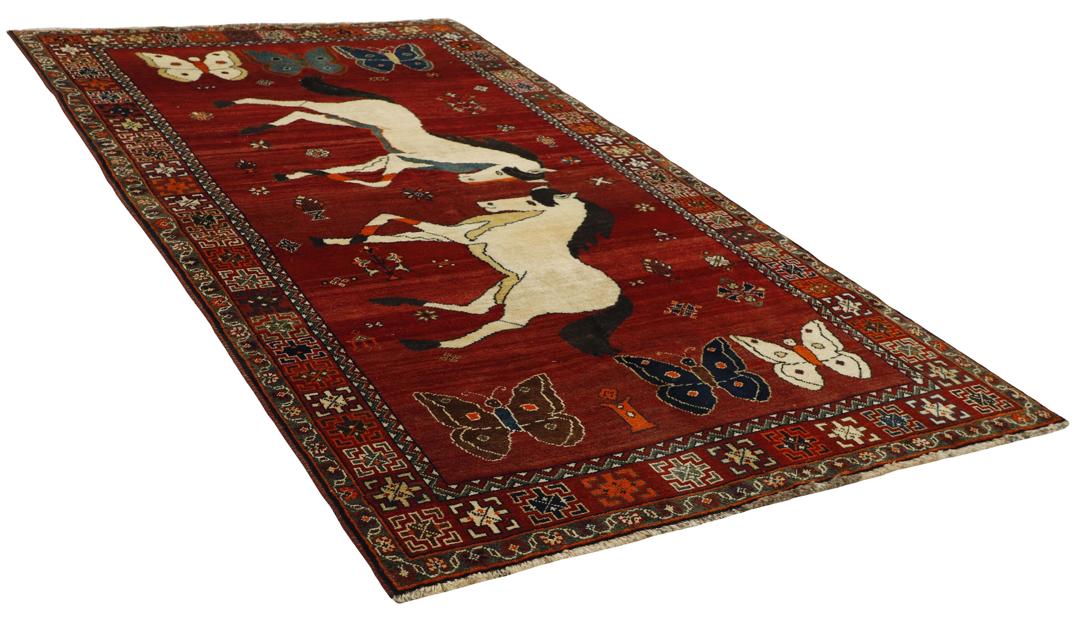 A hand-knotted Kashghai rug from the Middle East with a red field, featuring horse and butterfly motifs.