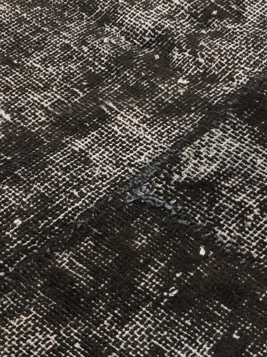 Een groot rechthoekig patchwork vloerkleed uit Turkije met een verweerd zwart en grijs patroon.