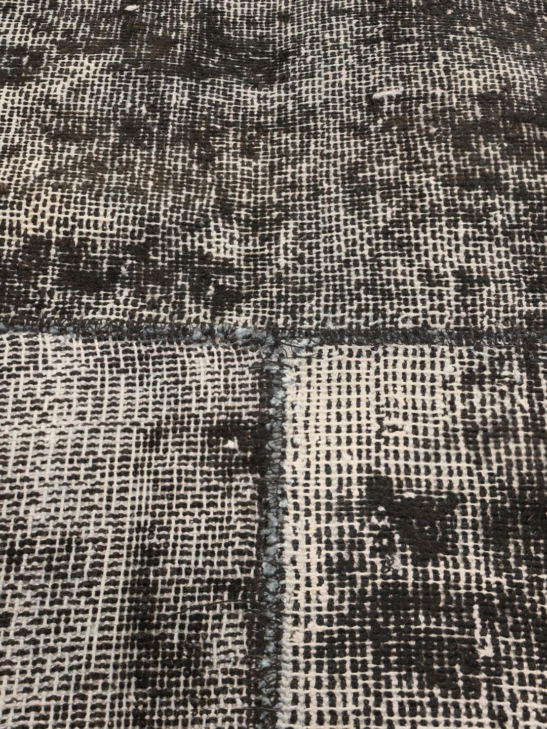 Een groot rechthoekig patchwork vloerkleed uit Turkije met een verweerd zwart en grijs patroon.