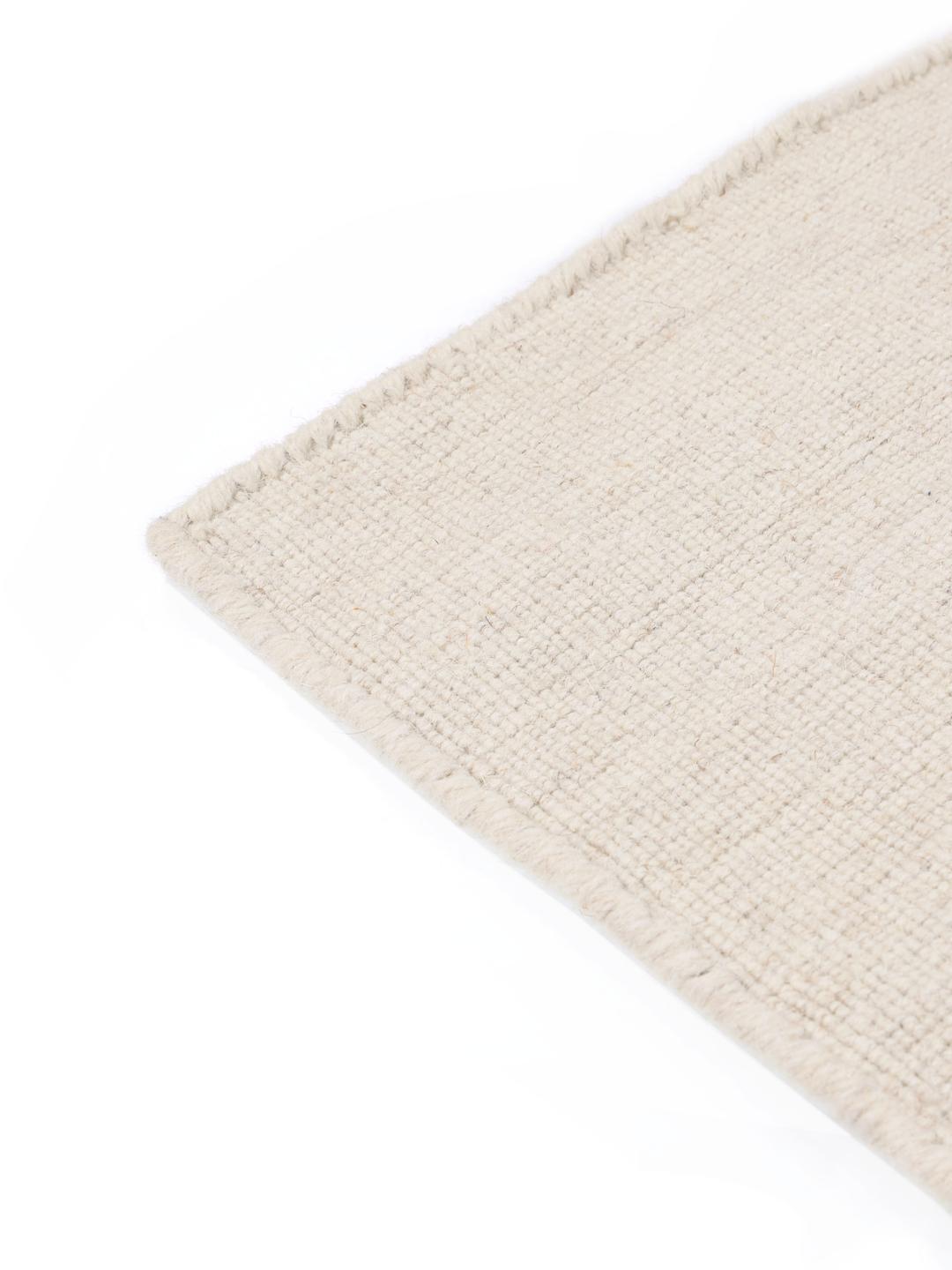 Håndvævet hvidt uldtæppe med en lav og flad tekstur.