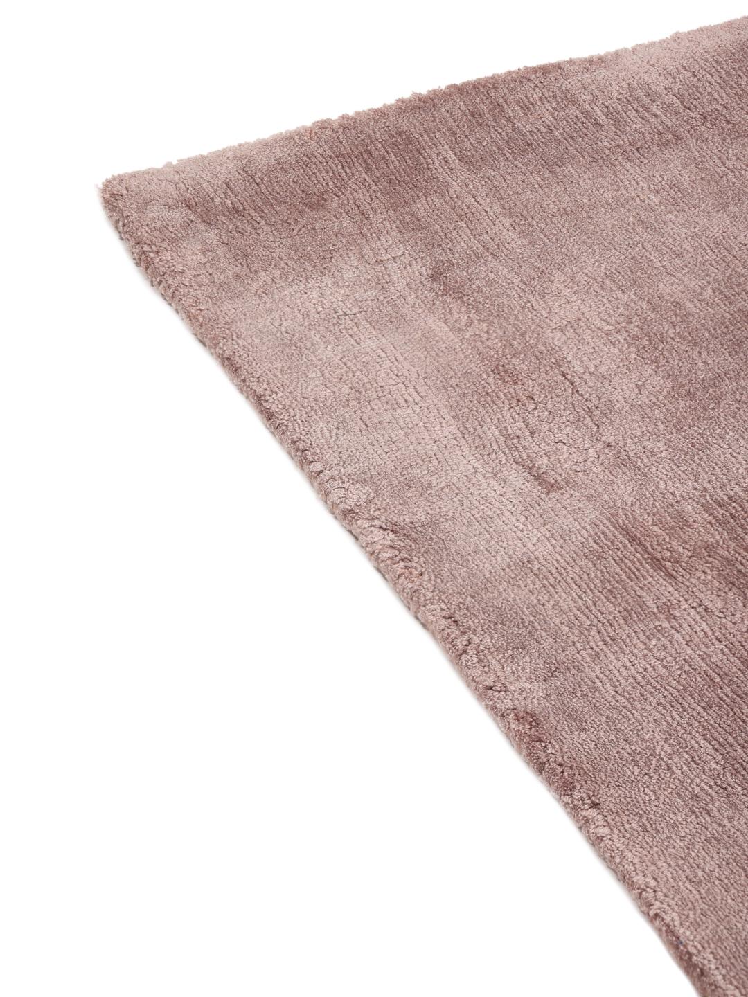 Een effen lichtroze tapijt met een zachte, lichtreflecterende textuur.