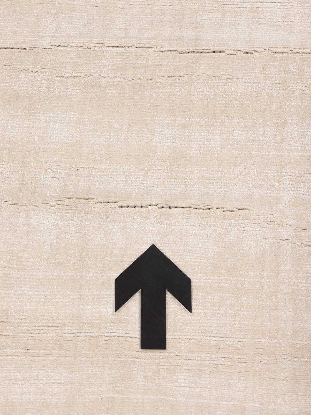 Square beige rug with minimalist dark arrow accents
